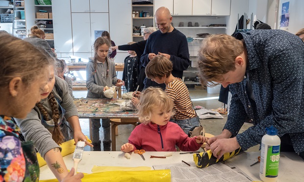 Children and adults paint and glue in a workshop. 